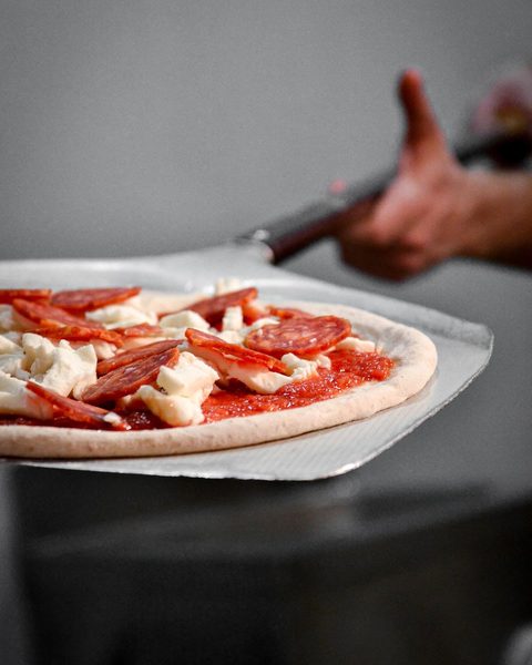 La pizza condita sulla pala, pronta per il forno